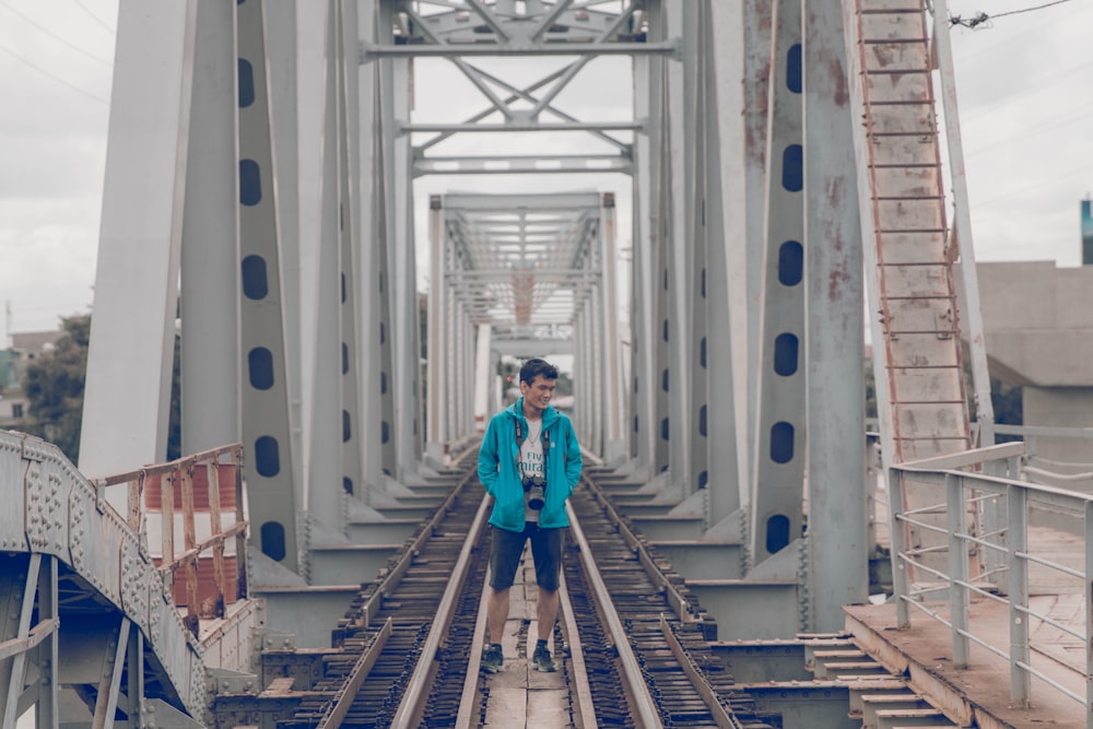 man wearing jacket standing on gray train bridge