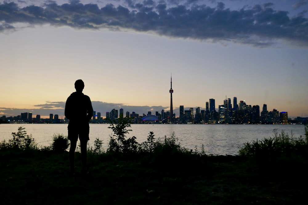 silhouette of a man standing on the grass in front of the city