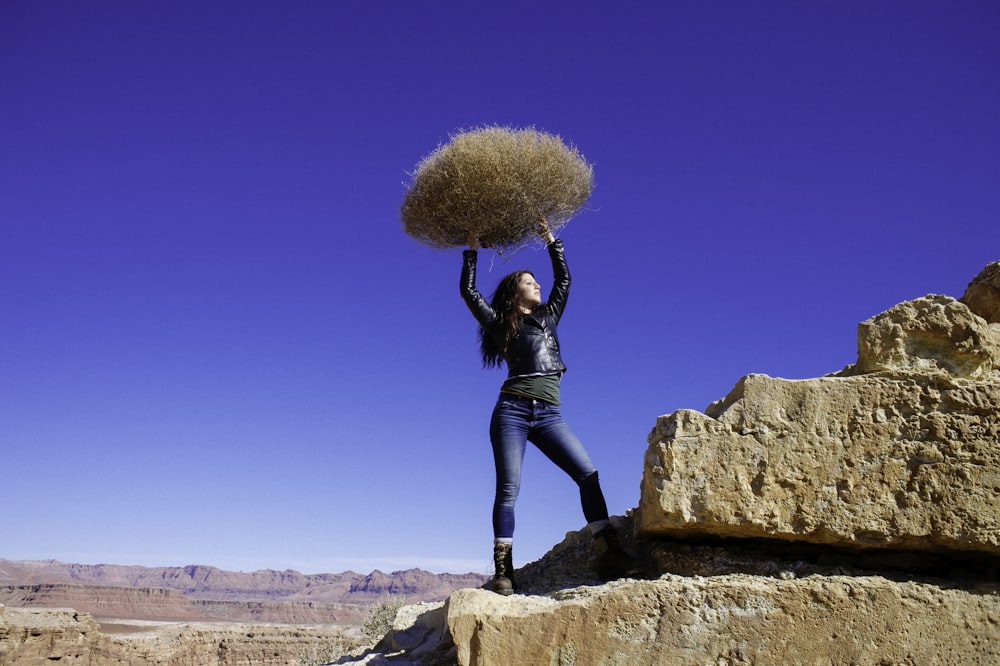 woman standing on rock formation while carrying hay during daytime