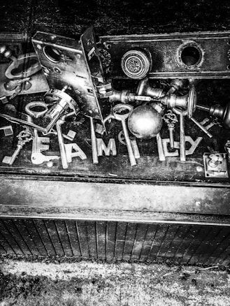 A collection of various keys and lock hardware is arranged on a dark surface. The word 'FAMILY' is spelled out using some of the keys. The image is in black and white, giving it a vintage and industrial feel.