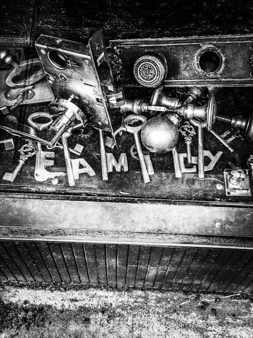A collection of various keys and lock hardware is arranged on a dark surface. The word 'FAMILY' is spelled out using some of the keys. The image is in black and white, giving it a vintage and industrial feel.