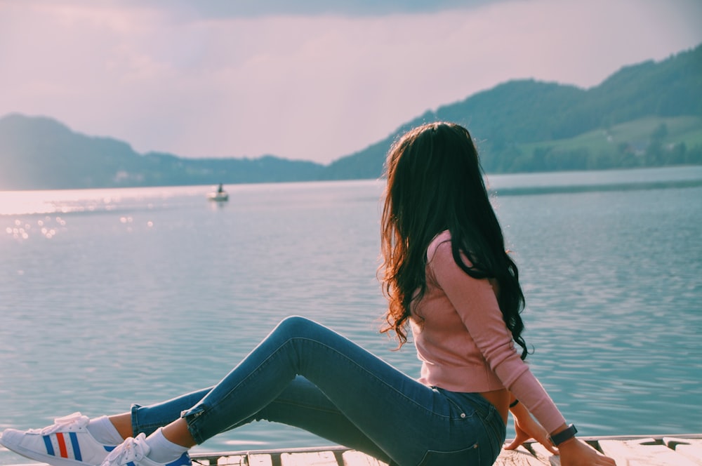 Frau sitzt auf dem Dock am Strand, während sie auf das Boot schaut