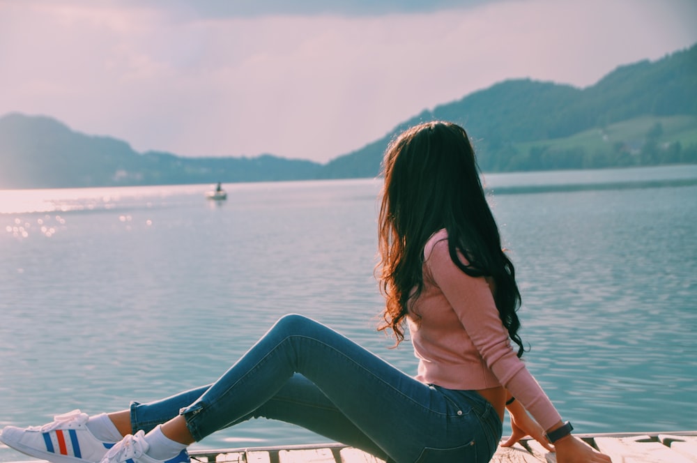 femme assise sur le quai de la plage tout en regardant sur le bateau