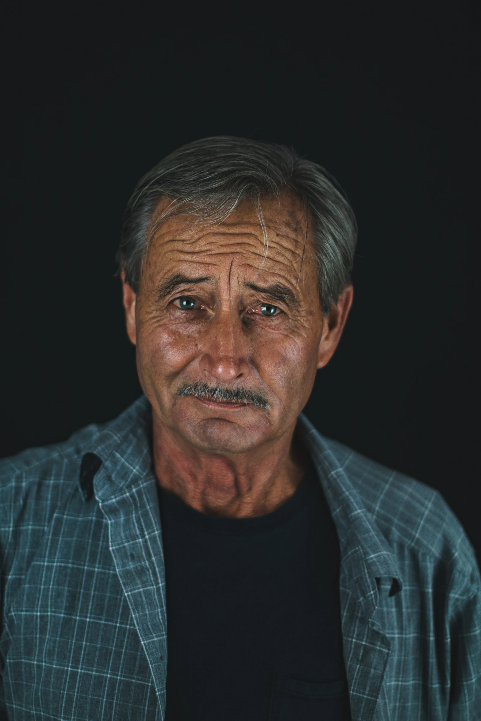 Distinguished gray-haired man in a blue collared shirt, editorial portrait.