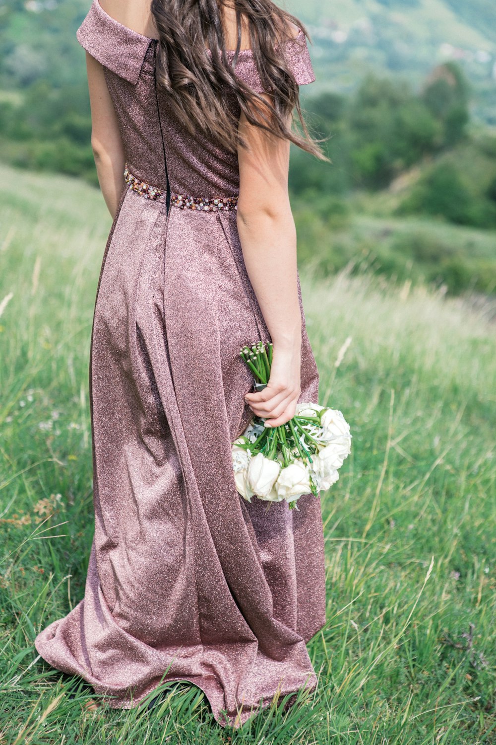 woman standing on grass fields holding bouquet of white flowers