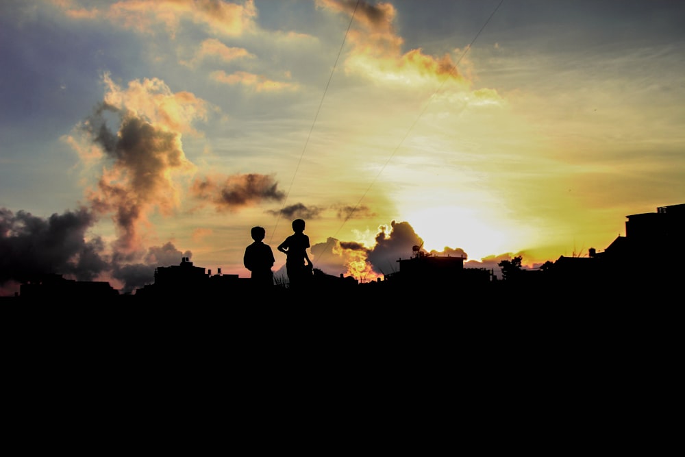 silhouette of two boys playing kites during golden hour