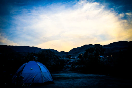 A rugged Ki'ler trekking pod pitched on a rocky hillside under a vibrant sunset.