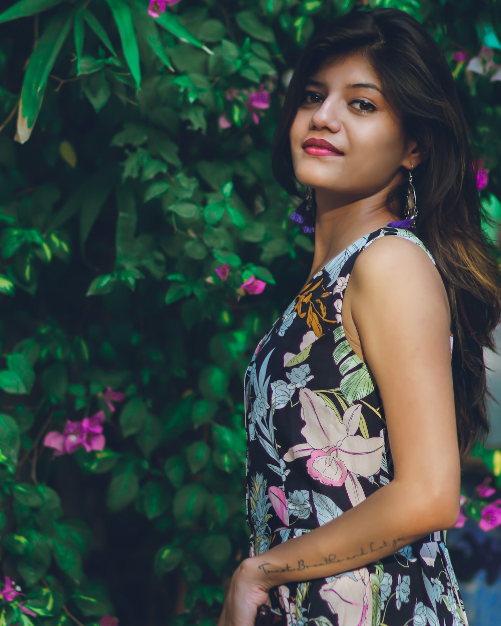 woman in black-and-multicolored floral tank dress standing beside pink petaled flowers