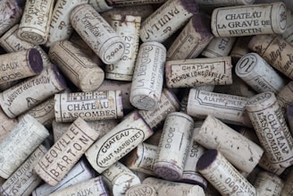 A collection of wine corks, featuring various imprints and labels from different châteaux and wineries. The corks are arranged in a random pile, with some displaying year markings and names.