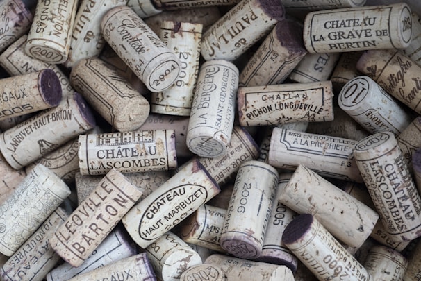 A collection of wine corks, featuring various imprints and labels from different châteaux and wineries. The corks are arranged in a random pile, with some displaying year markings and names.
