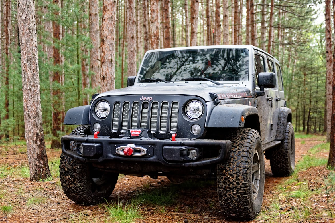 Jeep Wrangler with front hitch and American flag grille in the woods.