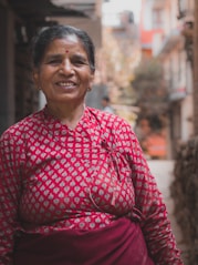 woman wearing red and grey long-sleeved floral dress smiling between buildings