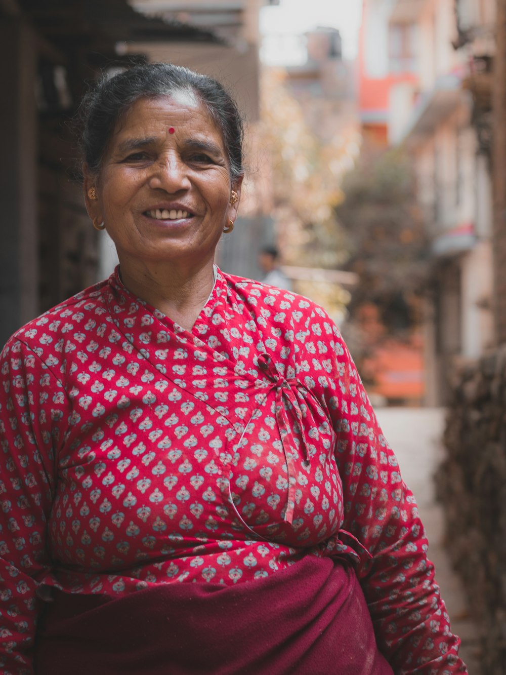 mujer con vestido floral de manga larga rojo y gris sonriendo entre edificios