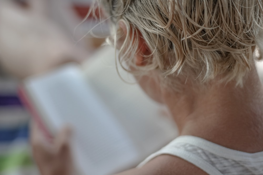 person in white tank top holding book