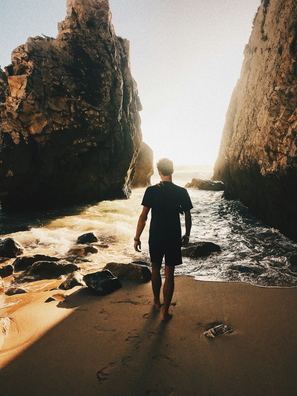 person standing on sand near seashore with rocks