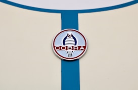A circular emblem featuring a stylized cobra design in blue and red is positioned on a cream-colored surface with a vertical blue stripe running through it.