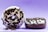 Two chocolate donuts with white icing and dark cookie crumb toppings are displayed against a gradient purple background. One donut is upright, leaning slightly on the other, while the second donut lies flat. Crumbs are scattered around the base, enhancing the sense of texture.