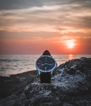 round silver-colored watch on rack during sunset