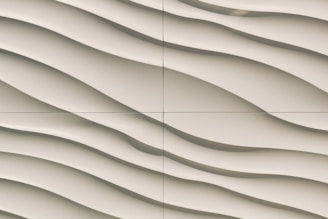 A close-up view of a textured wall featuring a series of smooth, wavy lines in a light beige color. The pattern gives a sense of flowing motion and adds a three-dimensional effect.