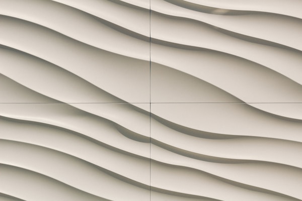 A close-up view of a textured wall featuring a series of smooth, wavy lines in a light beige color. The pattern gives a sense of flowing motion and adds a three-dimensional effect.