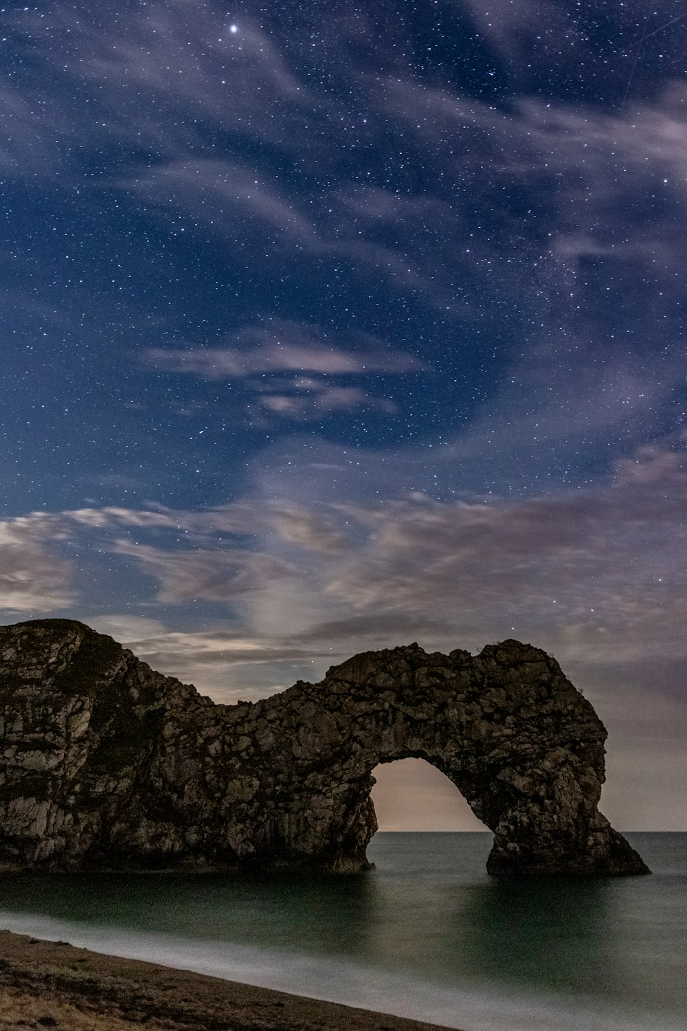 brown rock formation near shoreline at nighttime