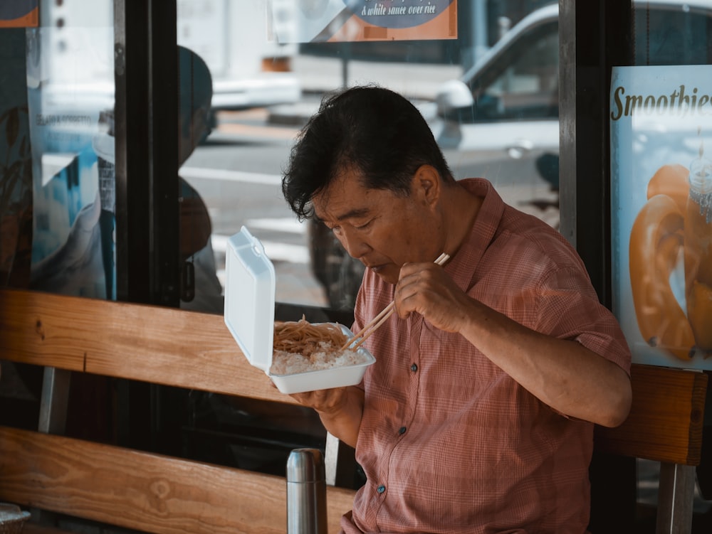 man sitting on brown wooden bench while eating