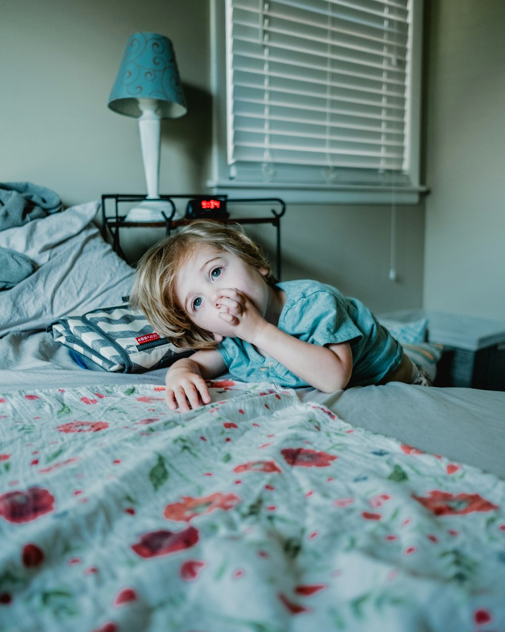 boy lying on bed while raising left hand near his mouth