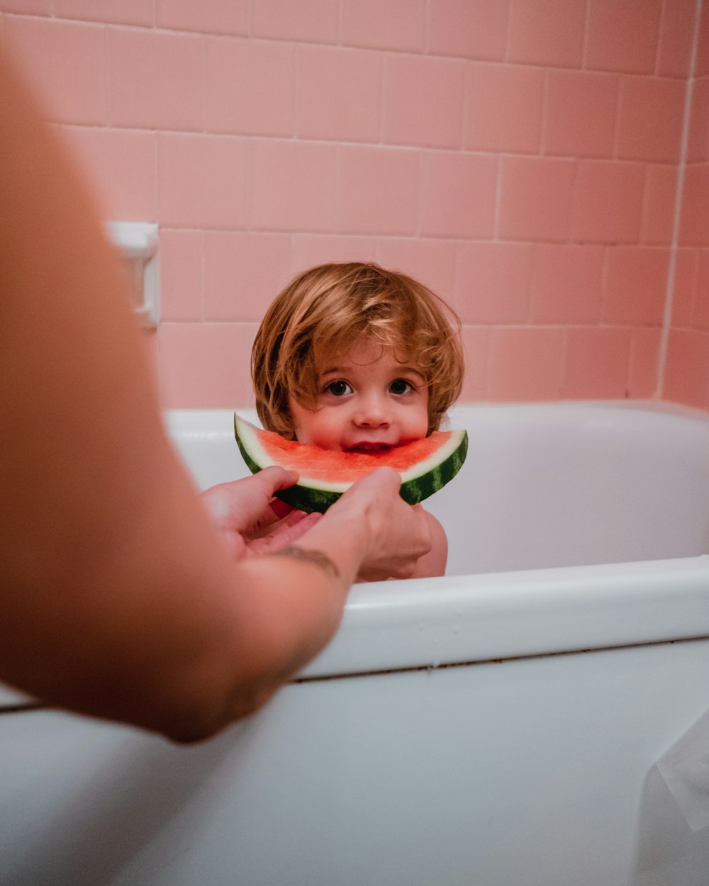 photo of boy in bathtub eating watermelon