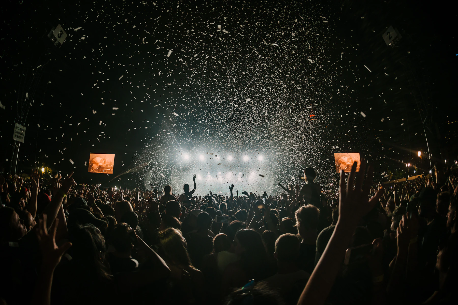 A festival crowd at night with confetti falling under stage lights
