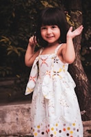 A young girl smiling while wearing a colorful summer dress outdoors.