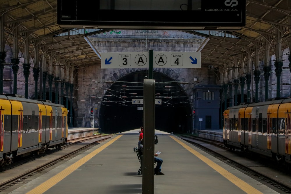 plusieurs personnes assises sur un banc entre deux trains qui passent à la gare