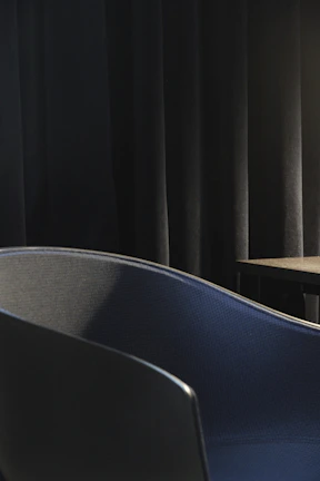 A sleek black blindfold draped over a vintage wooden chair in warm lighting.
