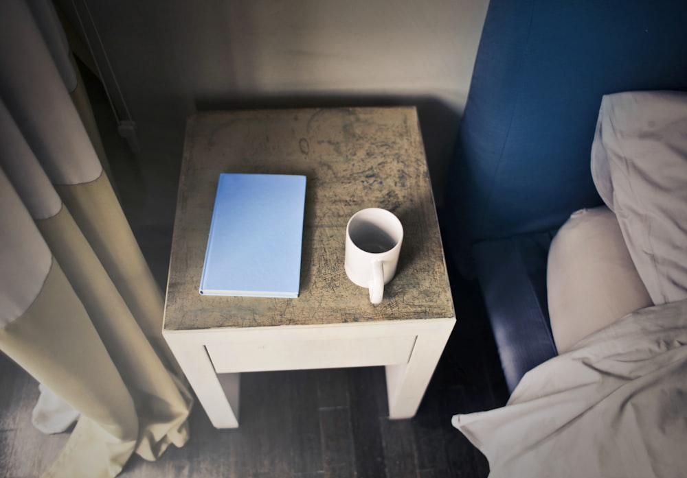 木製のテーブルの上の本の横の白いセラミックマグカップ