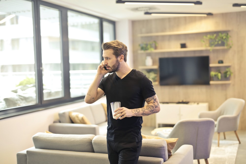 man holding drinking glass while taking a call on phone