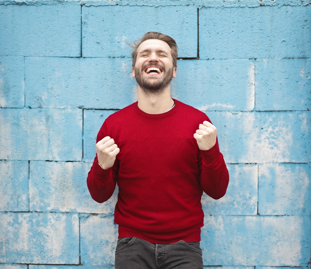 man wearing red long-sleeved shirt standing beside wall