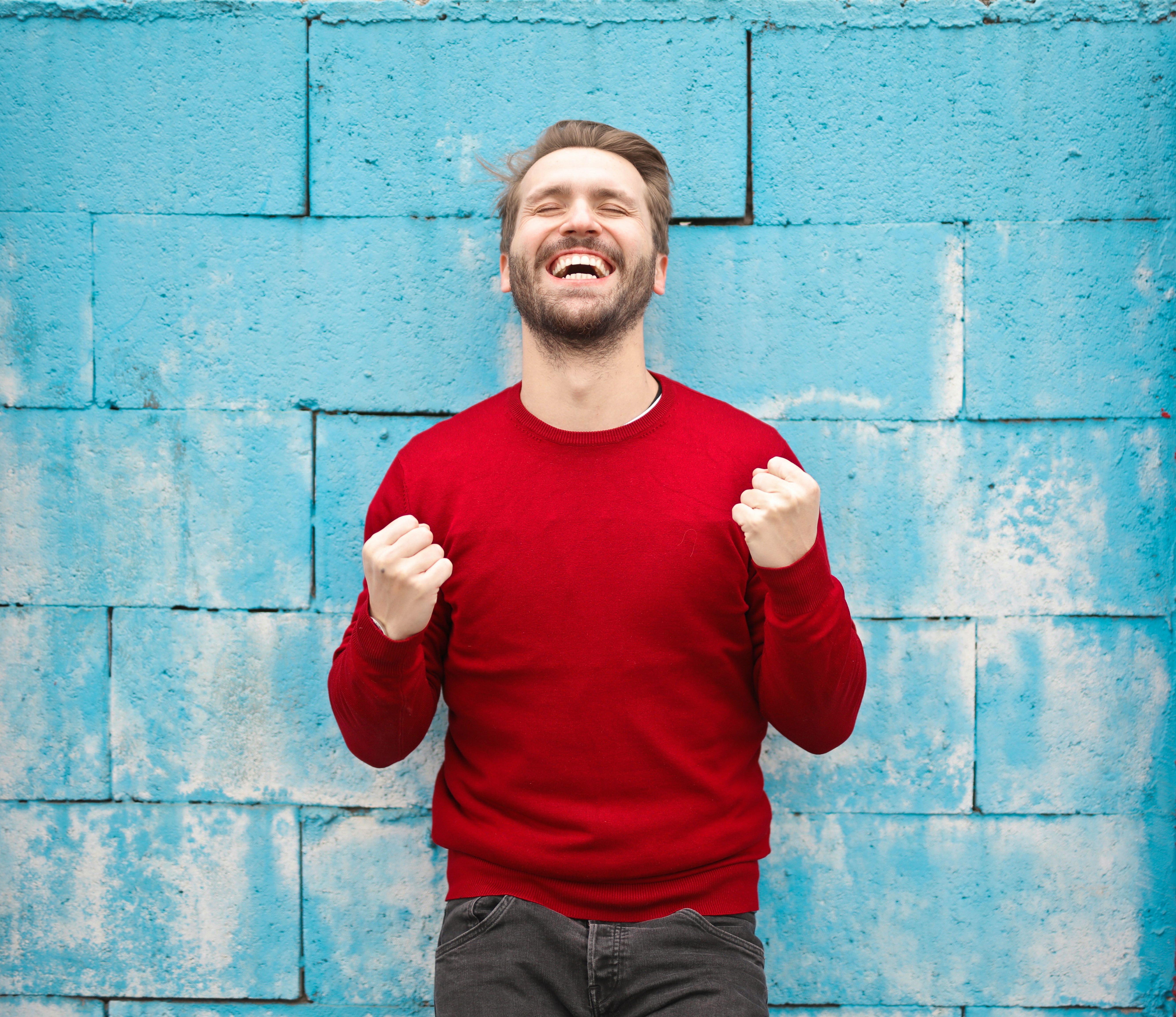 man wearing red long-sleeved shirt standing beside wall