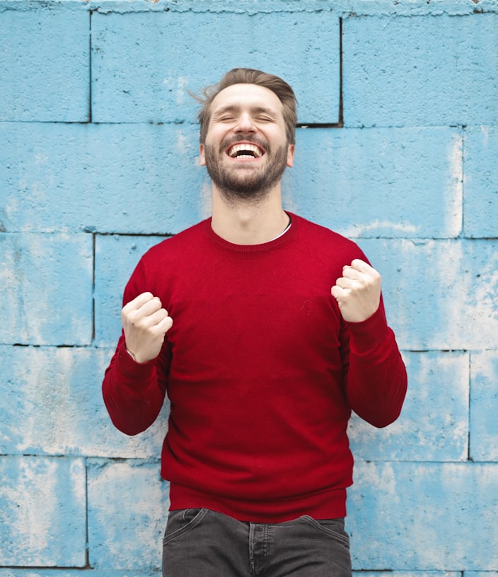 man wearing red long-sleeved shirt standing beside wall