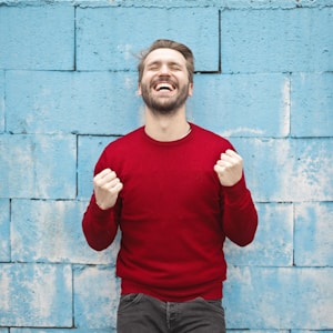 man wearing red long-sleeved shirt standing beside wall