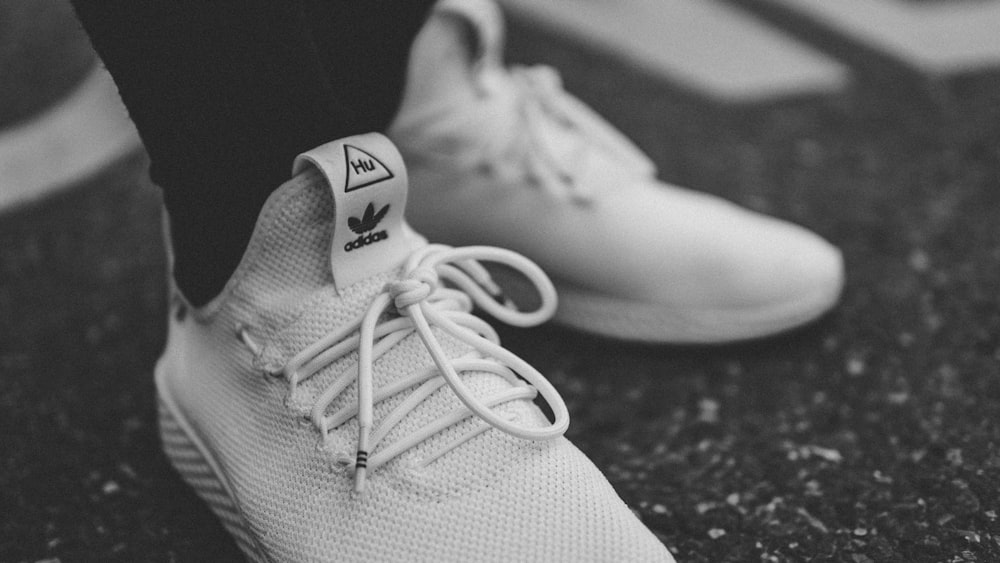 Foto en escala de grises de una persona con zapatillas blancas adidas de caña baja