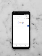 black Android smartphone showing google site on white surface