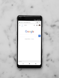 black Android smartphone showing google site on white surface
