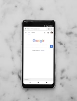 black Android smartphone showing google site on white surface