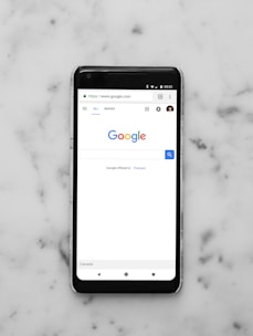 black Android smartphone showing google site on white surface