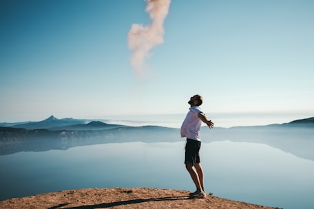 man standing on sand while spreading arms beside calm body of water