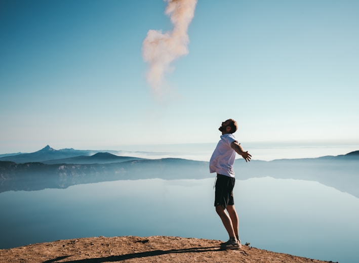 man standing on sand while spreading arms beside calm body of water