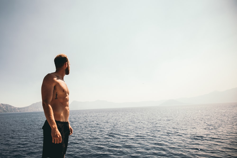 uomo che indossa pantaloncini neri in piedi vicino all'oceano