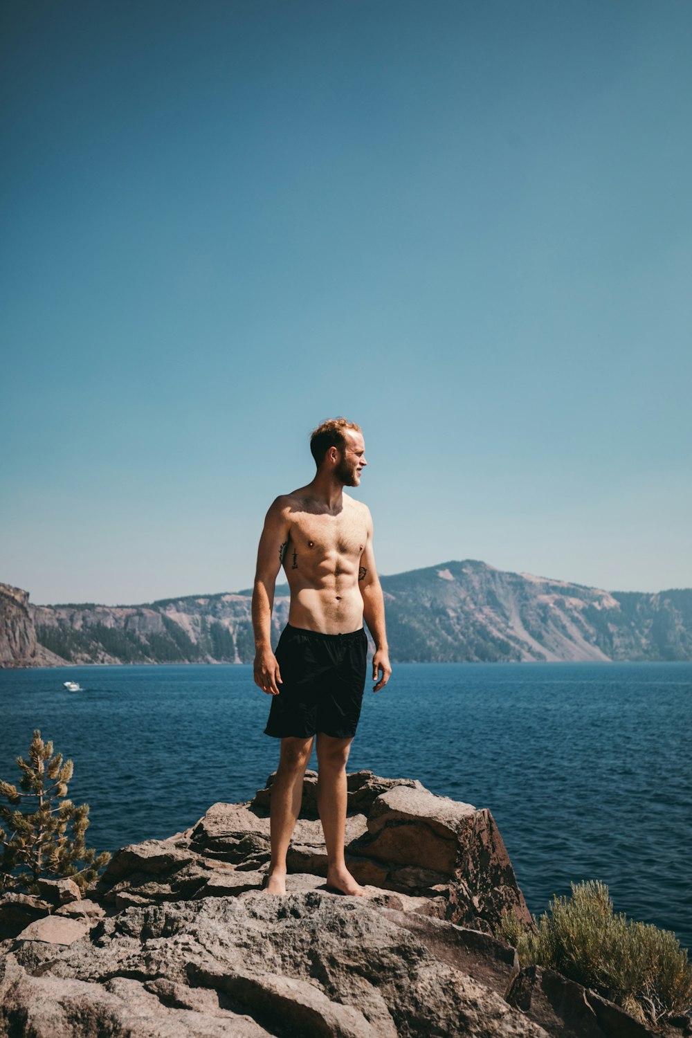 man standing on stone formation beside body of water