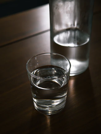 A sturdy glass bottle of still water resting on a wooden table with natural light.