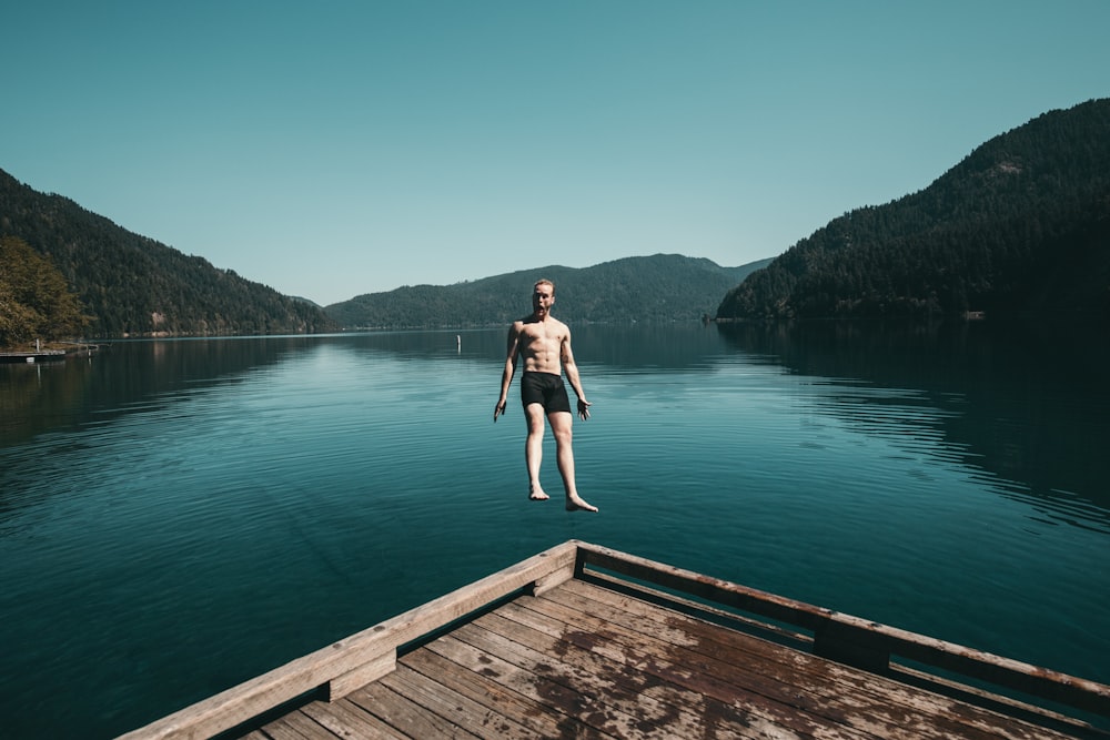 Mann springt rückwärts von brauner Holzplattform in den See