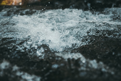 Water splashes energetically creating a textured surface with visible droplets and ripples. The movement suggests a flowing body of water with a dynamic and lively appearance.